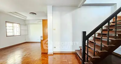 Spacious living area with wooden staircase and parquet flooring in a bright, open layout.