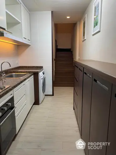 Modern kitchen with sleek cabinetry and built-in appliances, featuring a washing machine and stylish staircase.