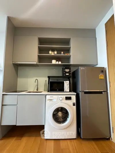Modern compact kitchen with washing machine, microwave, and fridge in sleek design.