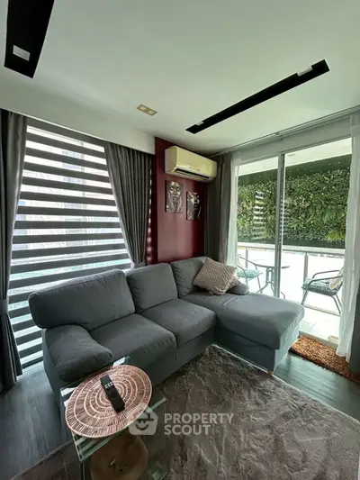 Modern living room with cozy gray sectional sofa and large windows opening to a lush balcony view.