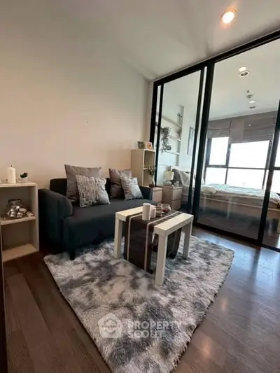 Modern living room with cozy decor and glass partition leading to bedroom