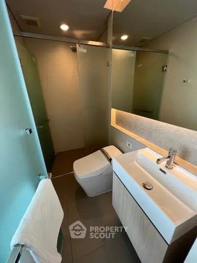 Modern bathroom with sleek fixtures and glass shower enclosure in contemporary apartment.