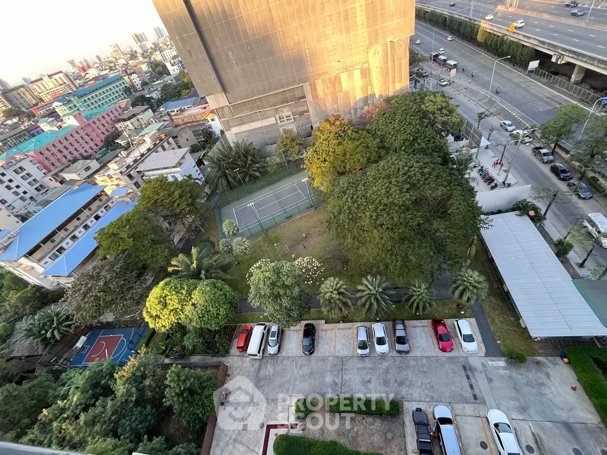 Stunning aerial view of urban residential area with lush greenery, tennis court, and ample parking space.