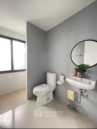 Modern bathroom with sleek design, featuring a round mirror and natural light from large window.