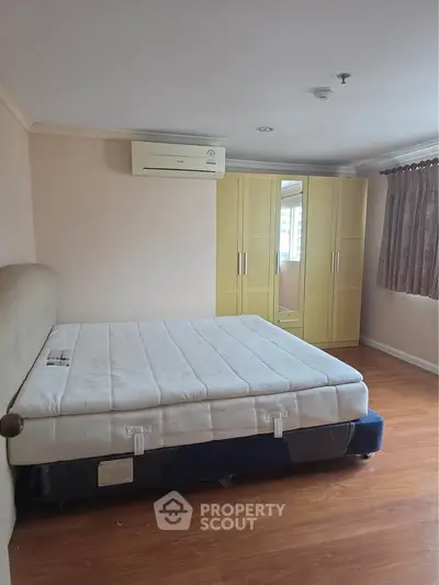 Spacious bedroom with hardwood floors, large wardrobe, and air conditioning unit.