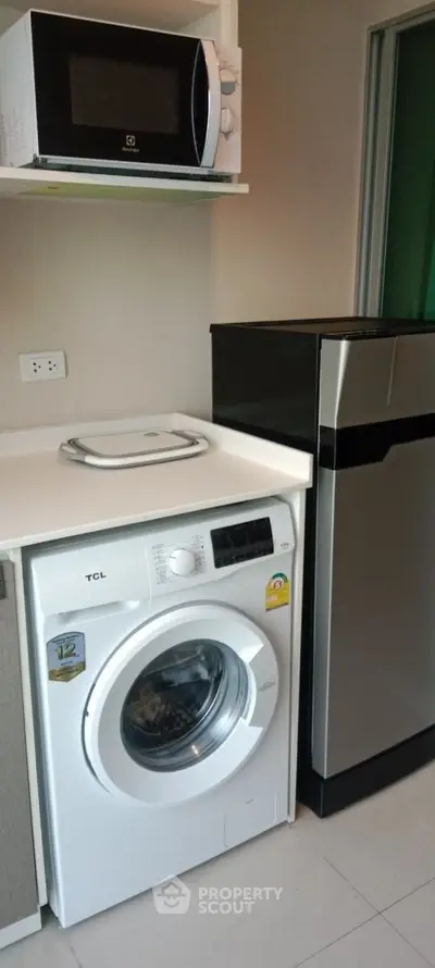 Modern kitchen with washing machine, microwave, and sleek refrigerator in compact layout.