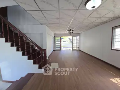 Spacious living room with wooden flooring and staircase, ample natural light.