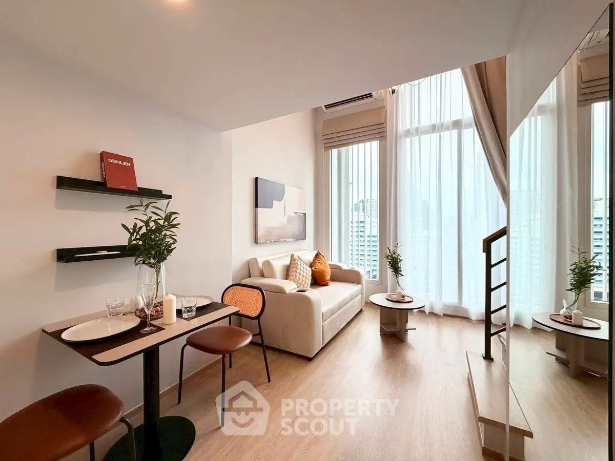 Modern living room with high ceilings and large windows offering city views, featuring stylish furniture and decor.