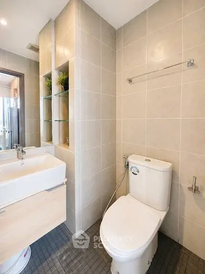 Modern bathroom with sleek fixtures and neutral tiles, featuring a stylish sink and toilet.