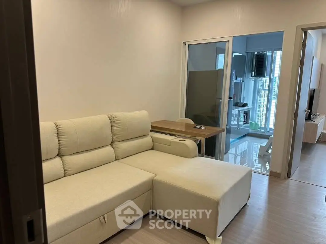 Modern living room with beige sectional sofa and glass sliding door leading to a bright balcony view.