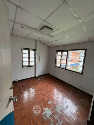 Spacious room with parquet flooring and large windows offering natural light.