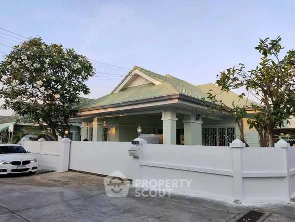 Charming single-story home with green roof and white fence in serene neighborhood.