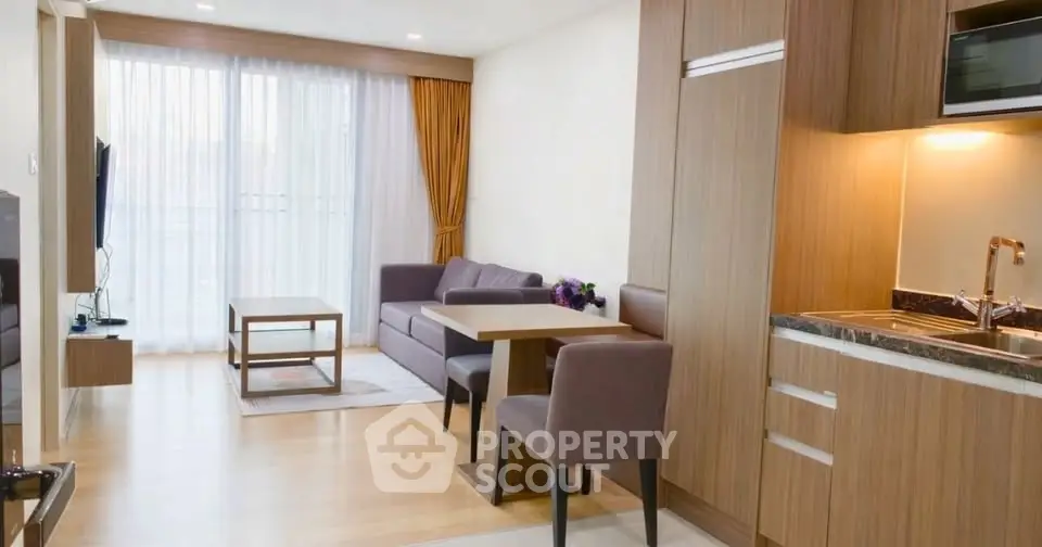 Modern living room with open kitchen, cozy seating, and natural light from large windows.