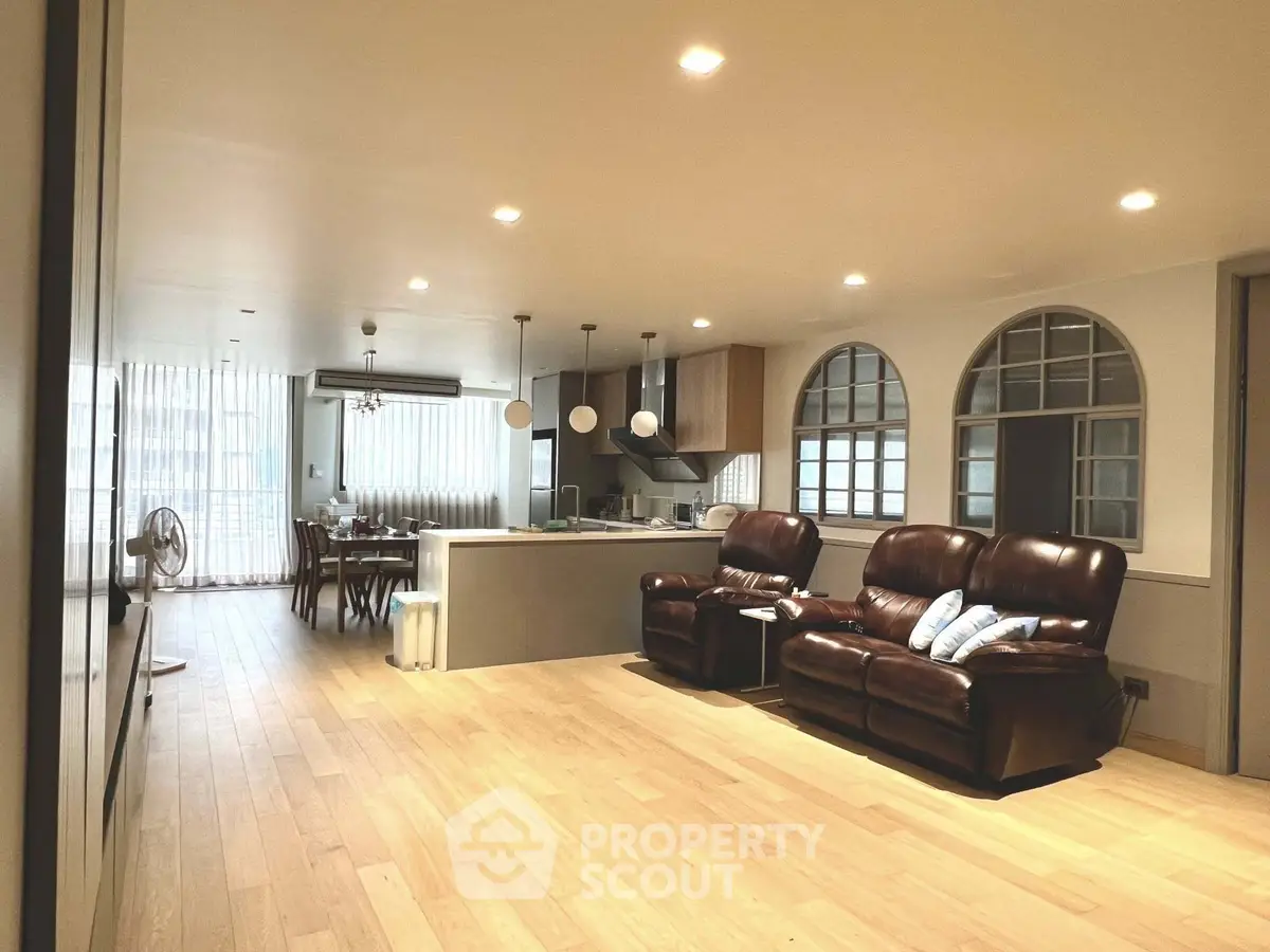 Spacious open-concept living room with modern kitchen and dining area, featuring elegant lighting and hardwood floors.