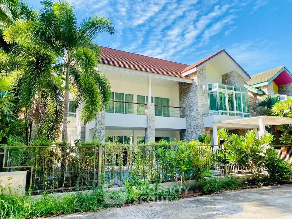 Luxurious tropical villa with lush garden and modern stone facade under clear blue sky.