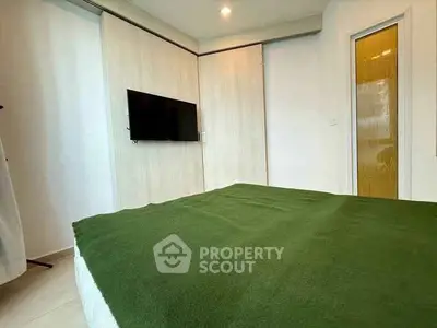 Modern bedroom with green bedspread and wall-mounted TV in stylish apartment.