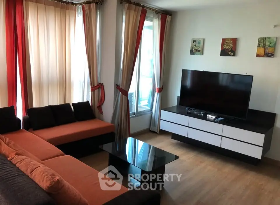 Modern living room with large TV, stylish sofa, and natural light from big windows.