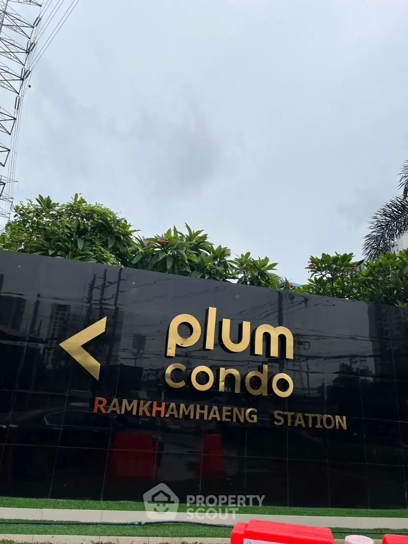 Plum Condo Ramkhamhaeng Station entrance sign with lush greenery.