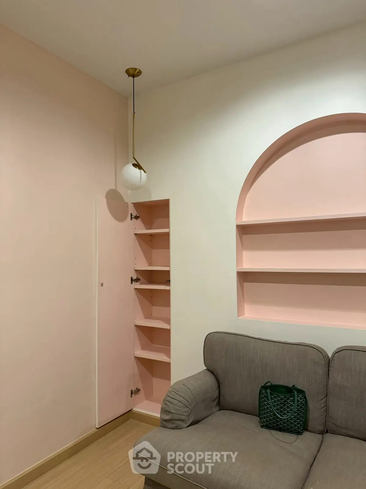 Charming living room with pastel pink shelves and cozy gray sofa, perfect for modern urban living.