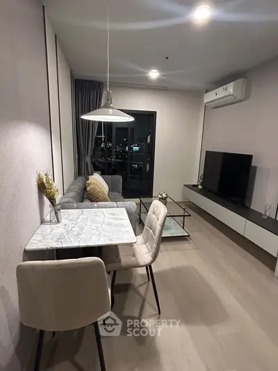 Modern living room with stylish furniture and city view, featuring a cozy dining area and sleek TV setup.