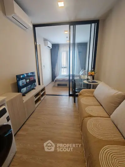 Modern apartment with cozy living room and bedroom separated by glass partition, featuring stylish decor and natural light.