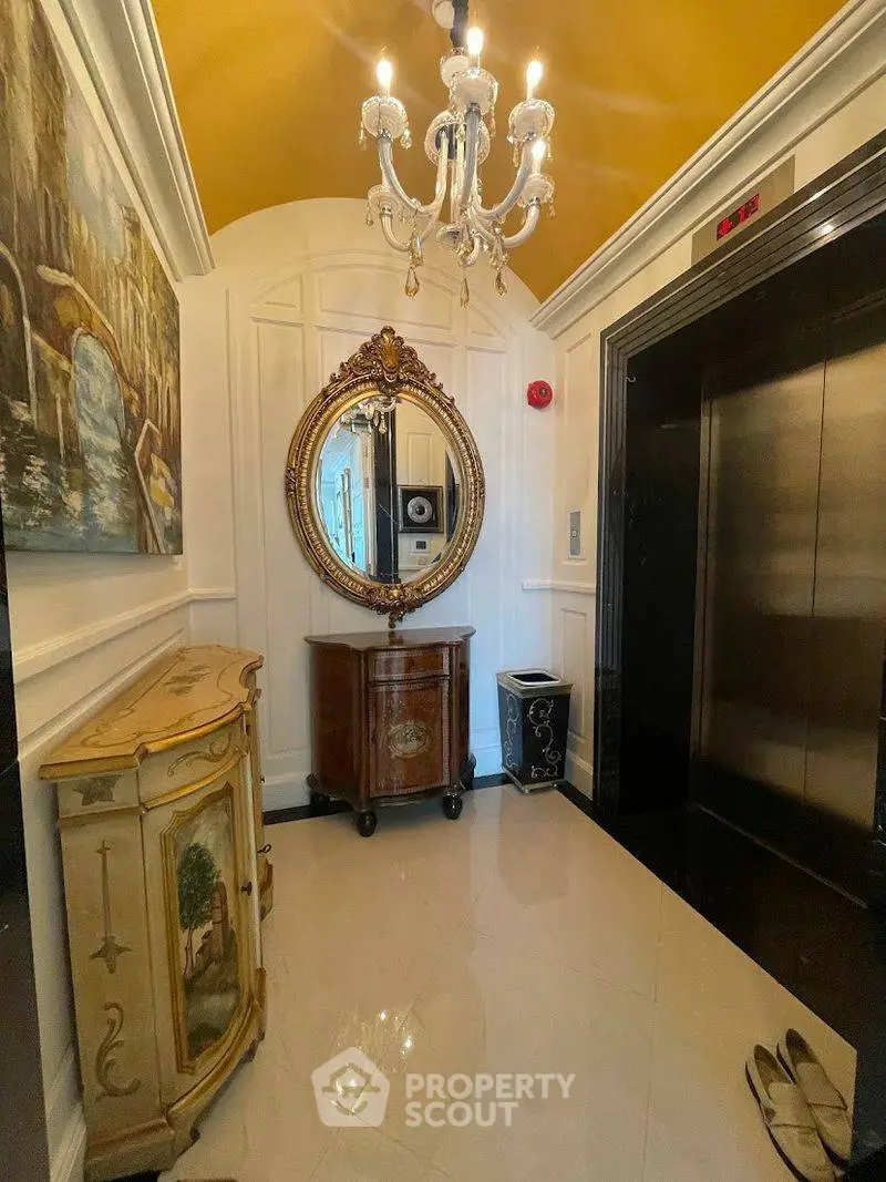 Elegant elevator lobby with chandelier and ornate mirror in luxury building.