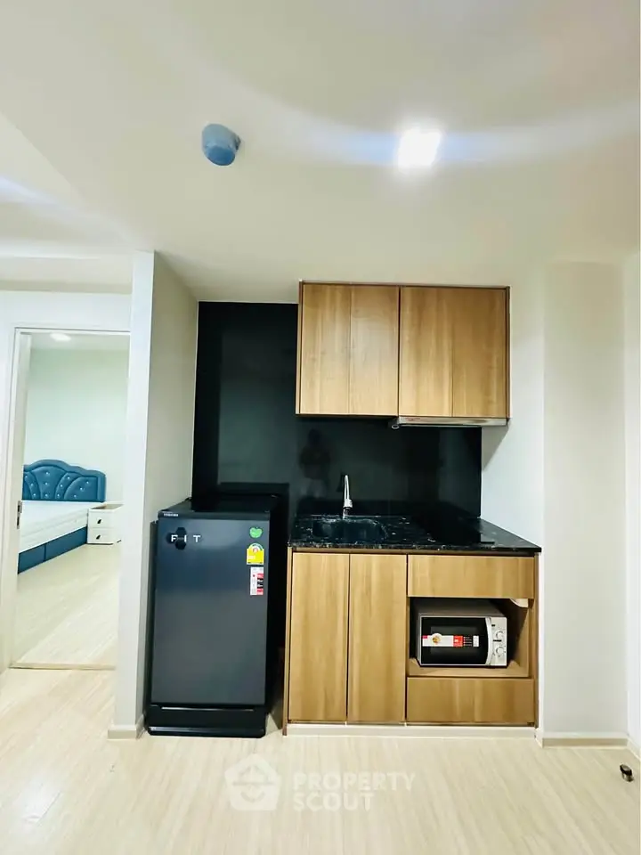 Modern compact kitchen with sleek wooden cabinets and black appliances in a cozy apartment setting.