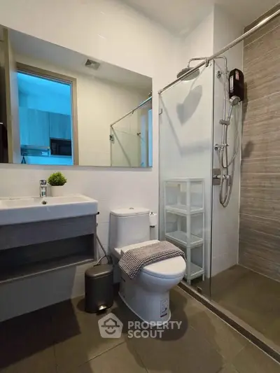 Modern bathroom with sleek fixtures and glass shower enclosure in contemporary apartment.