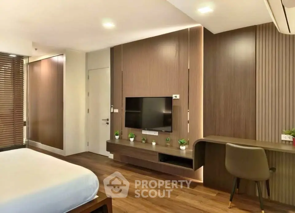 Modern bedroom with sleek wooden paneling and built-in TV, featuring a cozy workspace and stylish decor.