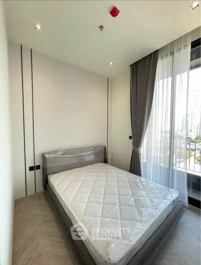 Modern bedroom with large window and city view, featuring a neatly made bed and elegant curtains.