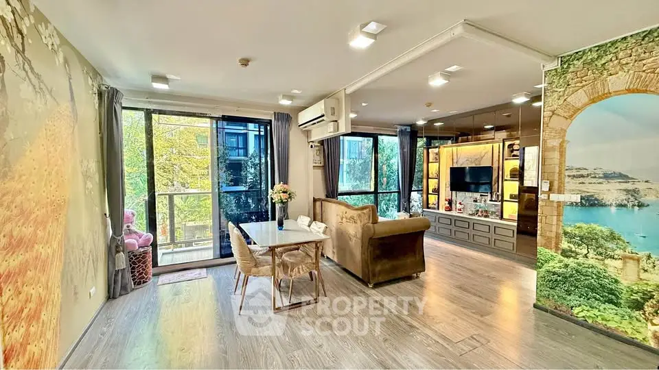 Spacious living room with large windows and scenic wall art, featuring modern furniture and natural light.