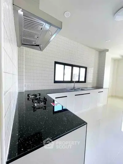 Modern kitchen with sleek black countertop and gas stove, featuring minimalist white cabinetry.