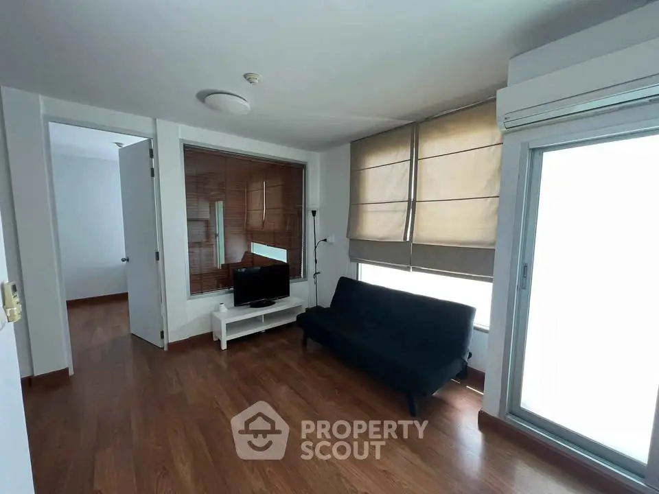 Cozy living room with wooden flooring, modern sofa, and natural light from large windows.