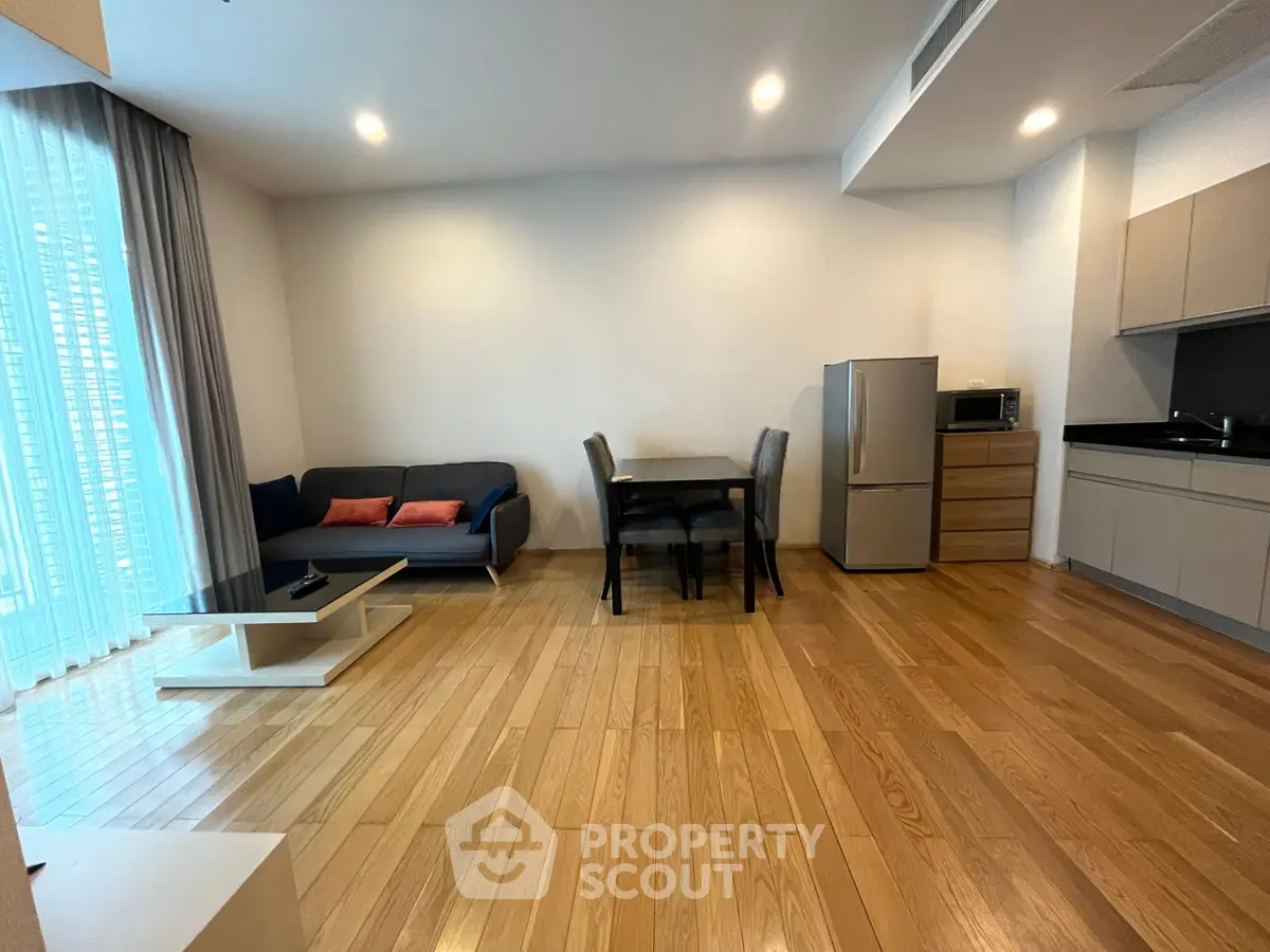 Modern open-layout living room with kitchen, featuring hardwood floors and stylish furniture.