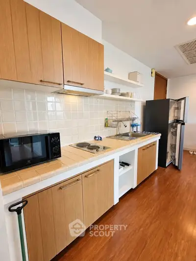 Modern kitchen with wooden cabinets and open shelving, featuring a microwave and refrigerator.