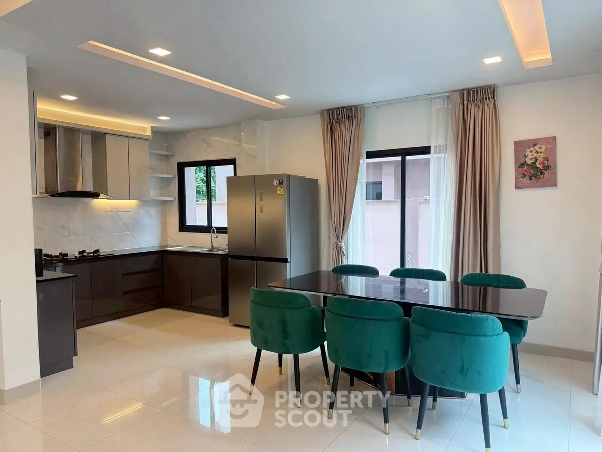 Modern kitchen with dining area, featuring sleek cabinetry and elegant green chairs.