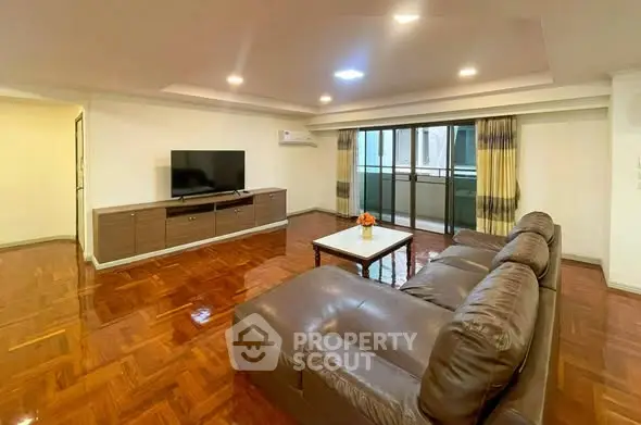 Spacious living room with modern furniture and large TV, featuring polished wooden floors.