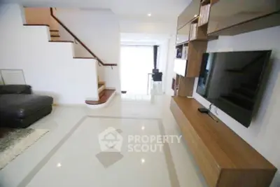 Spacious modern living room with sleek TV setup and elegant staircase.