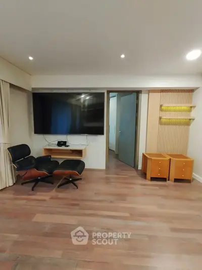 Spacious living room with modern decor and large wall-mounted TV, featuring elegant wooden flooring and stylish seating.