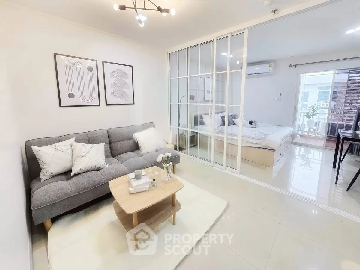 Modern open-plan living room with glass partition to bedroom, featuring stylish decor and natural light.