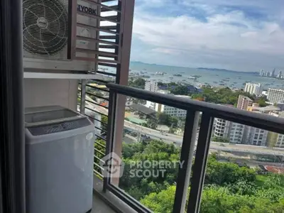 Stunning high-rise balcony view with lush greenery and ocean backdrop, featuring a compact washing machine.