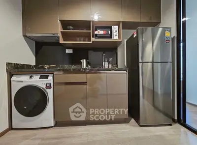 Modern kitchen with sleek cabinets, washing machine, microwave, and stainless steel fridge.