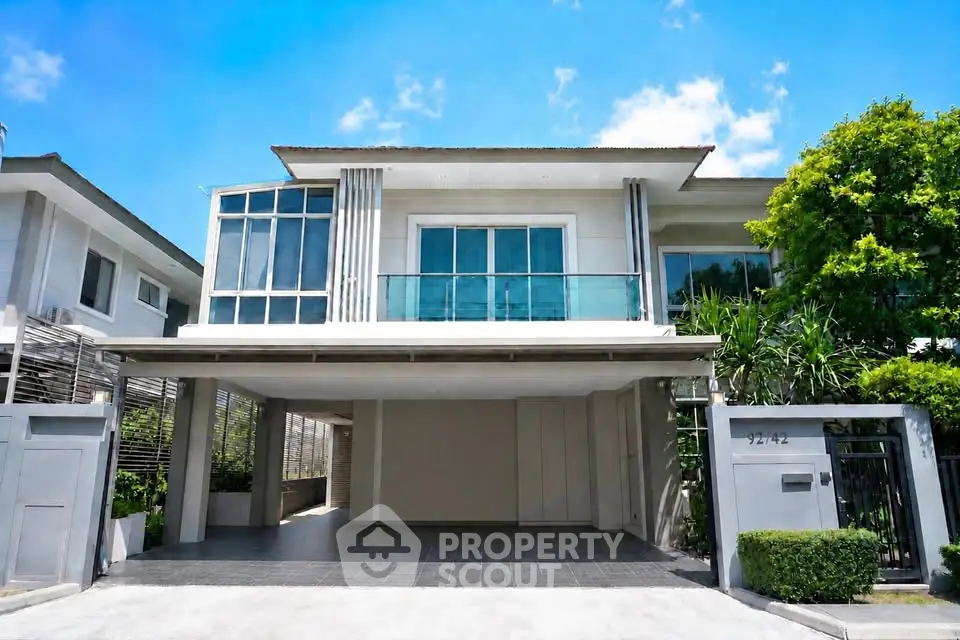 Modern two-story house with large windows and driveway in a sunny neighborhood.