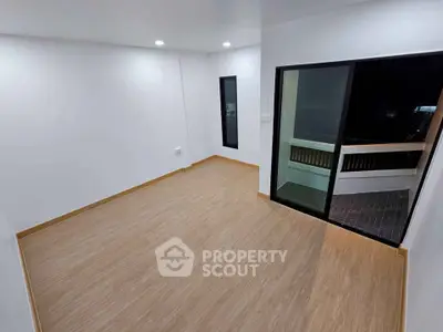 Spacious empty room with wooden flooring and sliding glass door leading to balcony.