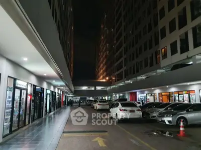 Modern building exterior with parking area and retail shops at night