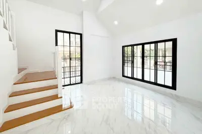 Bright and spacious living room with modern staircase and large windows.