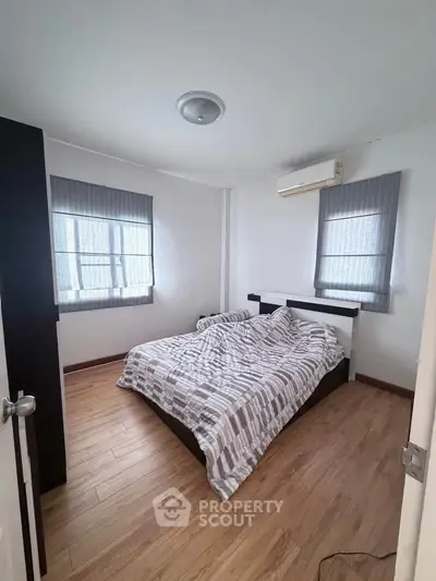 Cozy bedroom with wooden flooring and modern decor, featuring a comfortable bed and natural light.