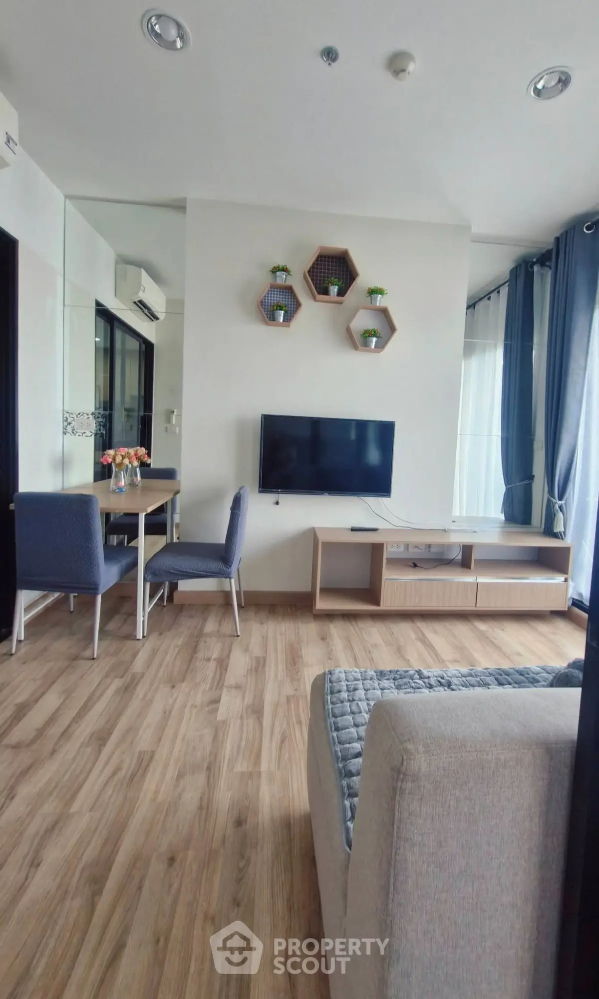 Modern living room with stylish decor and wooden flooring, featuring a wall-mounted TV and cozy seating area.