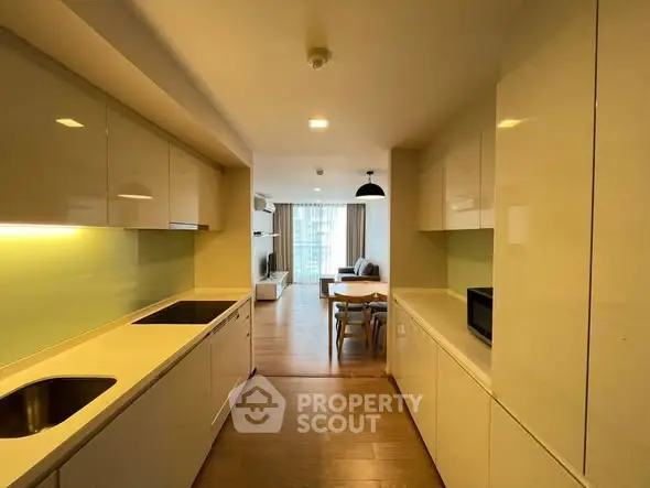 Spacious open-layout kitchen leading to a bright living room with modern furnishings and large windows.