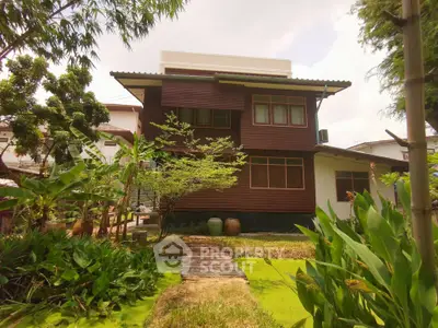 Charming two-story wooden house with lush garden and serene pond view.